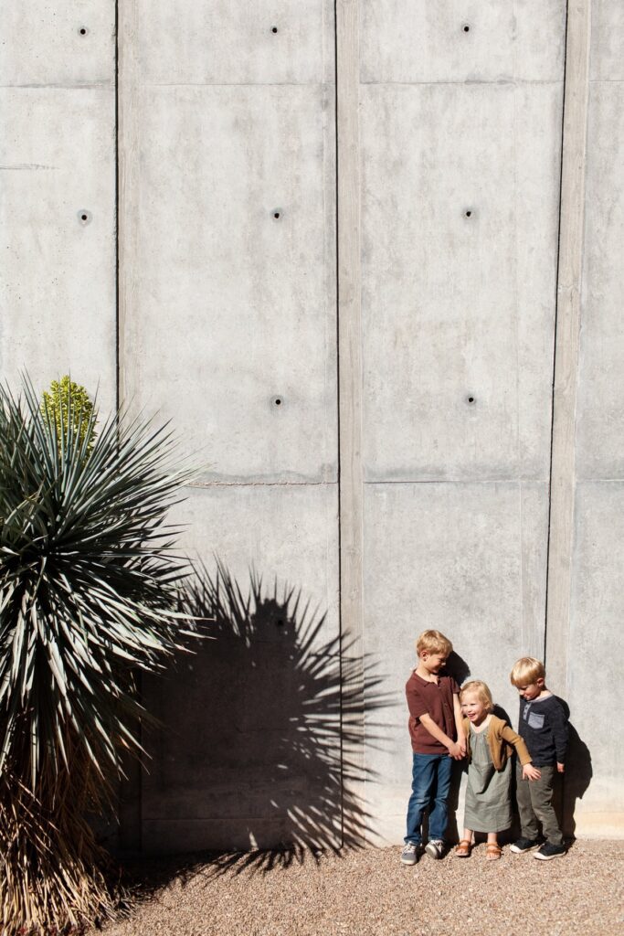 Three children standing in front of a concrete wall and laughing