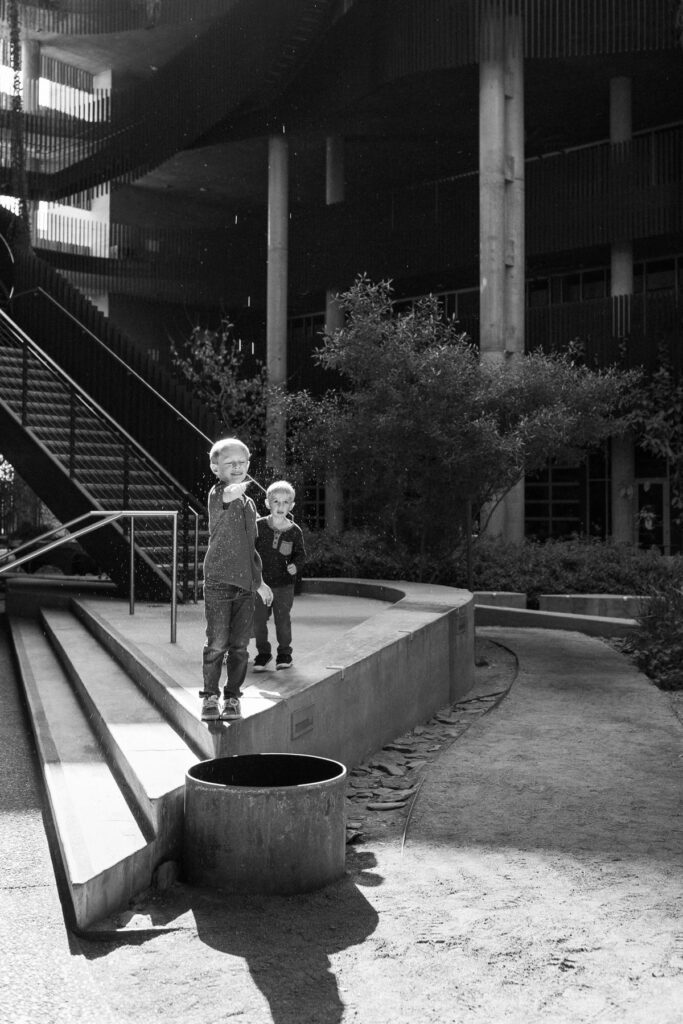 Two boys reaching for rain water dripping off of architectural building