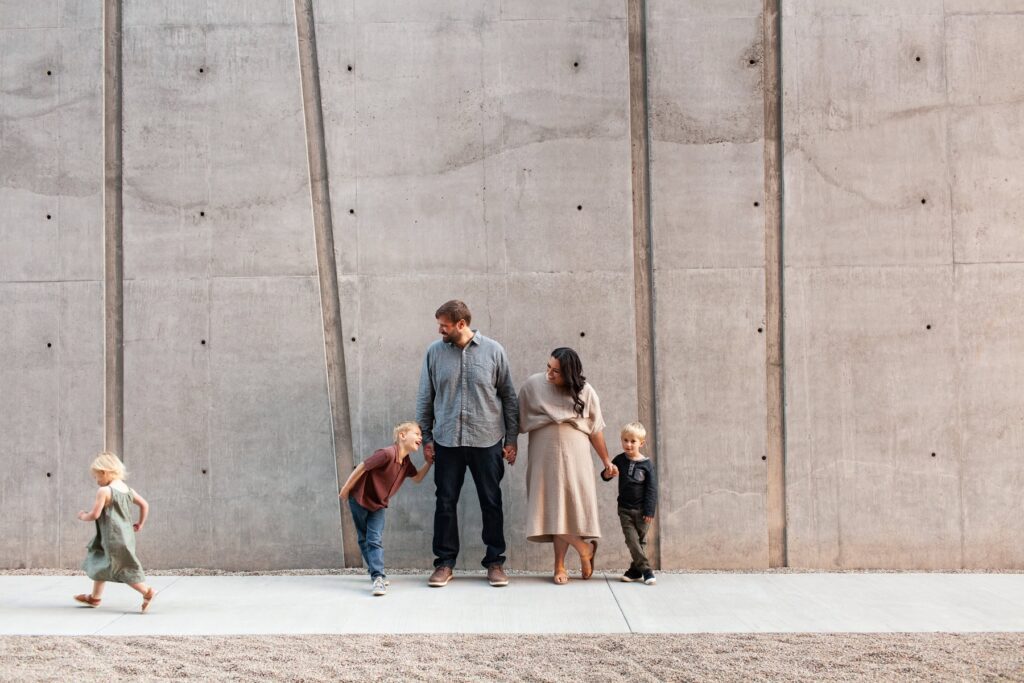 Family of five standing in front of a concrete wall watching their daughter run by during their architectural family portrait session