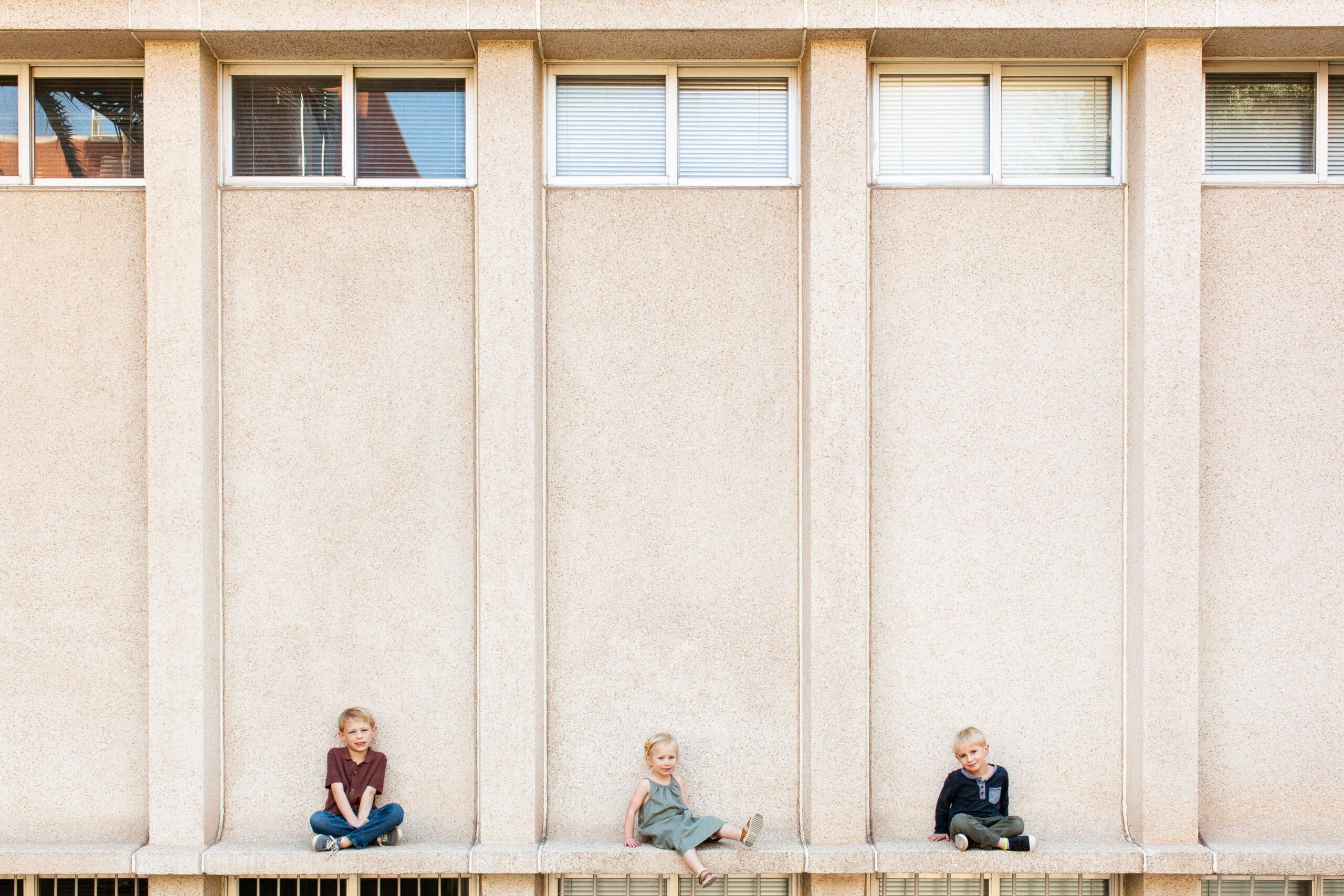 Architectural family portraits with young children smiling and sitting together on a concrete wall.